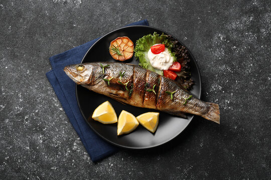 Plate With Delicious Sea Bass Fish And Ingredients On Dark Grey Table, Top View