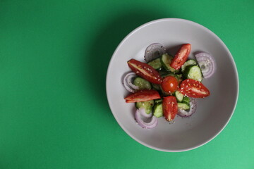 fresh vegetable salad tomatoes cucumber onions and honey mustard oil dressing in a gray plate on a green background with space for text and copyspace Useful healthy food