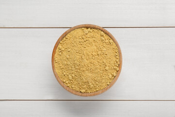 Bowl of aromatic mustard powder on white wooden table, top view