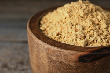 Bowl of mustard powder on wooden table, closeup