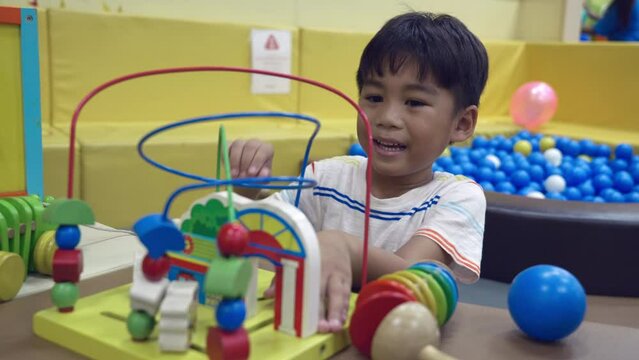 Happy Asian child man having fun on entertainment center play with the wried loop of wooden bead, excited boy playing wooden educational toy with looped wires for teaching coordination