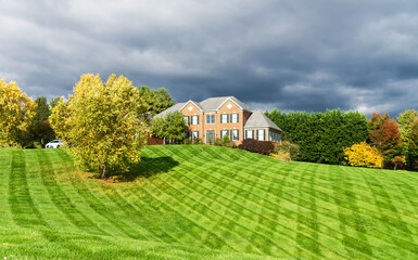 Country two-story brick house for one family with a large green lawn and shrubs. Landscape on an...
