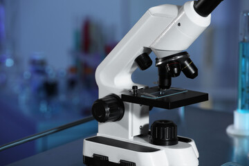Modern microscope with glass slide on metal table in laboratory, toned in blue. Space for text