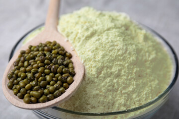 Bowl of flour, spoon and mung beans on light grey cloth, closeup