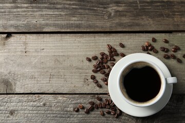 Cup of hot aromatic coffee and roasted beans on wooden table, flat lay. Space for text