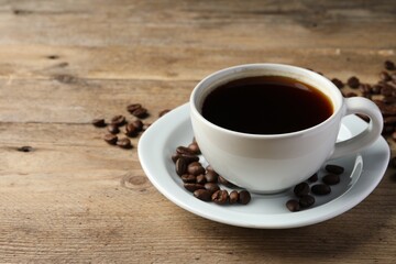Cup of hot aromatic coffee and roasted beans on wooden table, space for text