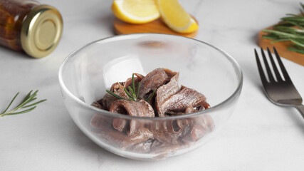 Canned anchovy fillets in glass bowl on white marble table
