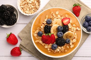 Delicious smoothie bowl with fresh berries, banana and oatmeal on white wooden table, flat lay
