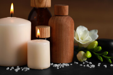 Fototapeta na wymiar Beautiful spa composition with different care products and burning candles on black table, closeup