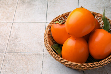Delicious ripe juicy persimmons in wicker basket on tiled surface, space for text