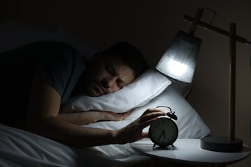 Sleepy man turning off alarm clock on nightstand in morning