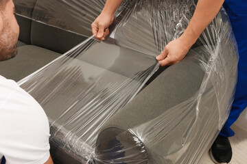 Workers wrapping sofa in stretch film indoors, closeup
