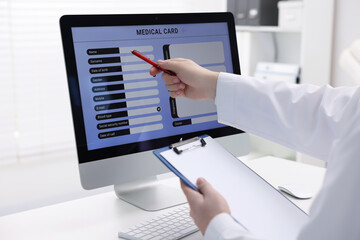 Doctor using computer to fill out patient's medical card at table in clinic, closeup