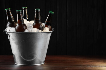 Metal bucket with bottles of beer and ice cubes on wooden table, space for text - obrazy, fototapety, plakaty