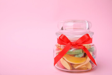 Tasty colorful jelly candies in glass jar on pink background. Space for text