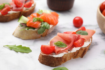 Different tasty bruschettas on white marble table, closeup