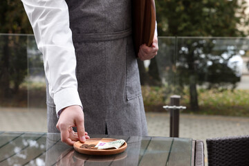 Waiter taking tips from wooden table in outdoor cafe, closeup