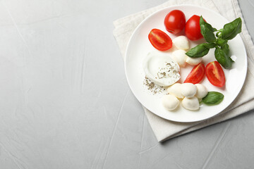 Delicious mozzarella with tomatoes and basil leaves on light gray table, top view. Space for text