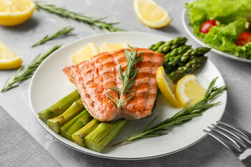 Tasty grilled salmon with asparagus, lemon and rosemary on light grey table