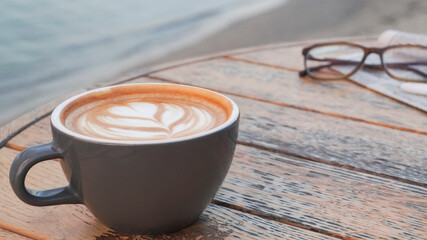Cup of delicious coffee, eyeglasses and newspaper on wooden table, closeup. Space for text