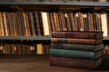 Many stacked hardcover books on wooden table in library, space for text