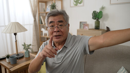senior Japanese grandfather talk on video call with relatives on cellphone while face camera as lens. happy elderly man having online conversation with kid and reminding them with health point finger