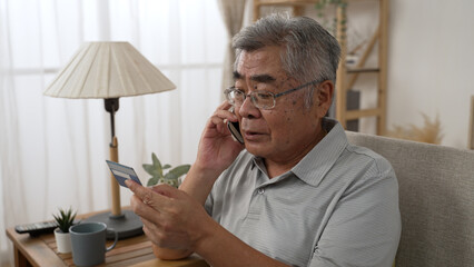 Sad old asian man with credit card call bank support by cellphone reporting about money fraud. senior male telling problem on smartphone while taking debit card. elderly grandpa talk on mobile phone