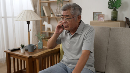 senior man sitting on home sofa and answering call on cellphone during retirement time. boring...