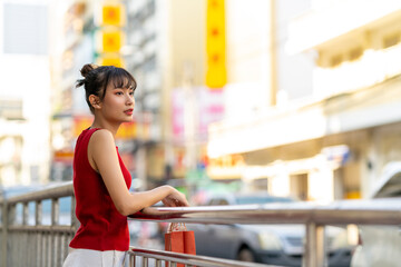Portrait of Happy Young Asian woman holding red shopping bag during buy home decorative ornaments and joss paper for celebrating Chinese Lunar New Year festive at Bangkok Chinatown street market.