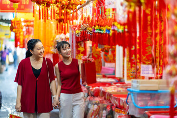Asian woman mother and daughter holding shopping bag during buy home decorative ornament for celebrating Chinese Lunar New Year festival at Bangkok Chinatown street market. Chinese culture concept.