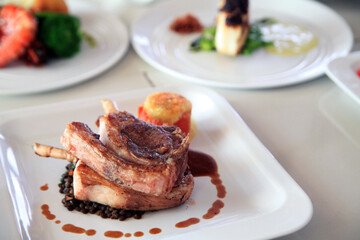 expensive grilled lamb chop ribs on square white plate with other food at background 