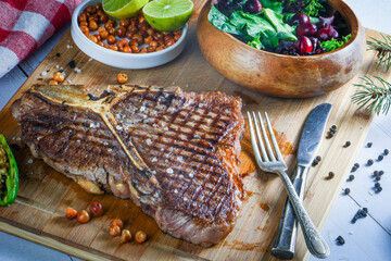 Grilled t-bone or porterhouse steak seasoned with rosemary in a rustic kitchen on a wooden board with salad