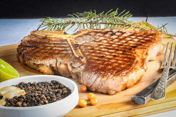 Grilled t-bone or porterhouse steak seasoned with rosemary in a rustic kitchen on a wooden board with pepper