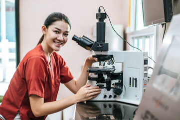 Asian young female farmer looking through a microscope in a laboratory. Modern technologies in agriculture management, agribusiness and research concept.
