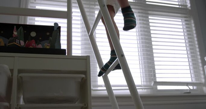 Young boy climbs up ladder into bunk bed during day - close up on ladder