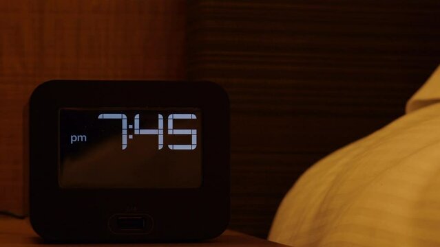 Close up of electronic alarm clock stands on a bedside table in the room. 