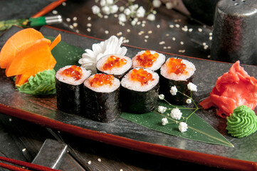 Sushi rolls with salmon and hot tea ceremony on black wooden table