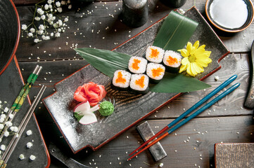Sushi rolls with salmon and hot tea ceremony on black wooden table