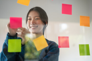 Confident businesswoman planning while looking at adhesive notes stuck on a glass wall.