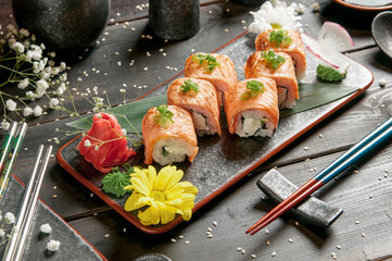 Sushi rolls with salmon and hot tea ceremony on black wooden table