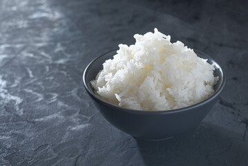 Cooked rice in a black cup on black table as background.