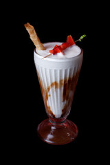 Vanilla milkshake with strawberry garnish black background close up