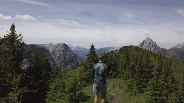 Hiker walking trough pine trees on mountain range descending birds flying over head Rockies Kananaskis Alberta Canada