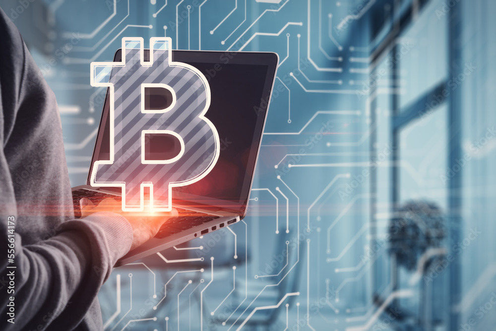 Poster close up of hand using laptop with glowing bitcoin hologram on blurry office interior background. di