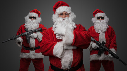 Studio shot of santa posing with crossed arms and two santa with rifles standing on his sides.