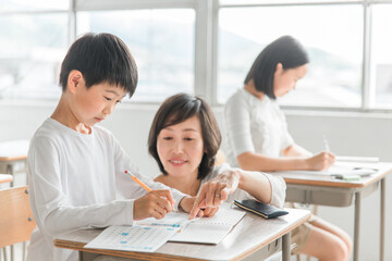 学校の教室・塾で先生と話す高学年のアジア人男子生徒（学習・教育）
