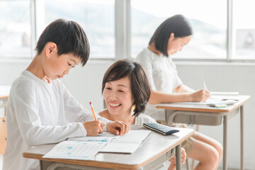 Fototapeta premium 学校の教室・塾で先生と話す高学年のアジア人男子生徒（学習・教育） 