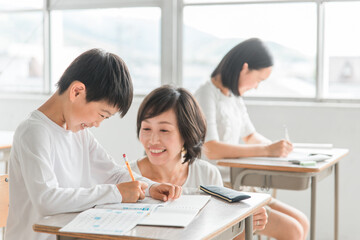 学校の教室・塾で先生と話す高学年のアジア人男子生徒（学習・教育）
