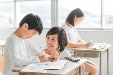 学校の教室・塾で先生と話す高学年のアジア人男子生徒（学習・教育）
