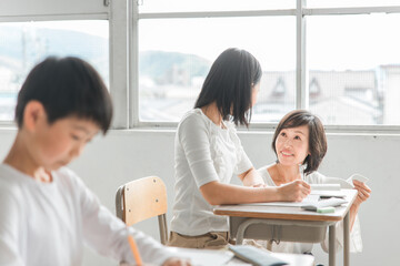 学校の教室・塾で先生と話す高学年のアジア人女子生徒（学習・教育）
